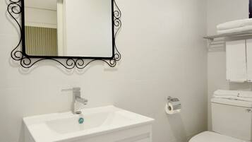A bathroom with a white sink, a mirror with an ornate black frame, a toilet, and a towel rack.