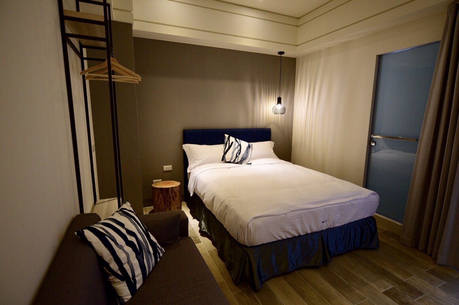 Une chambre à coucher avec un lit, un banc en bois, une petite table ronde et un luminaire suspendu.