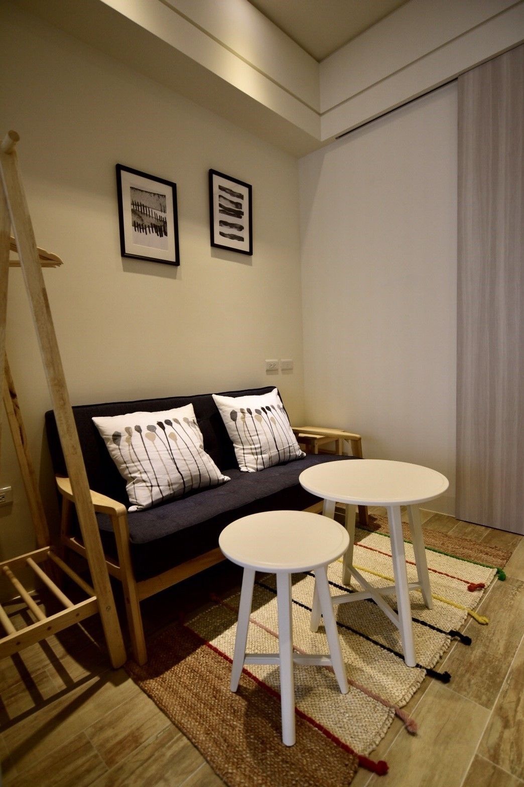 A modern living room with a dark sofa, two white round tables, and a wooden ladder leaning against the wall.