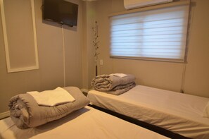 A hotel room with two beds, a TV mounted on the wall, and a window with blinds.