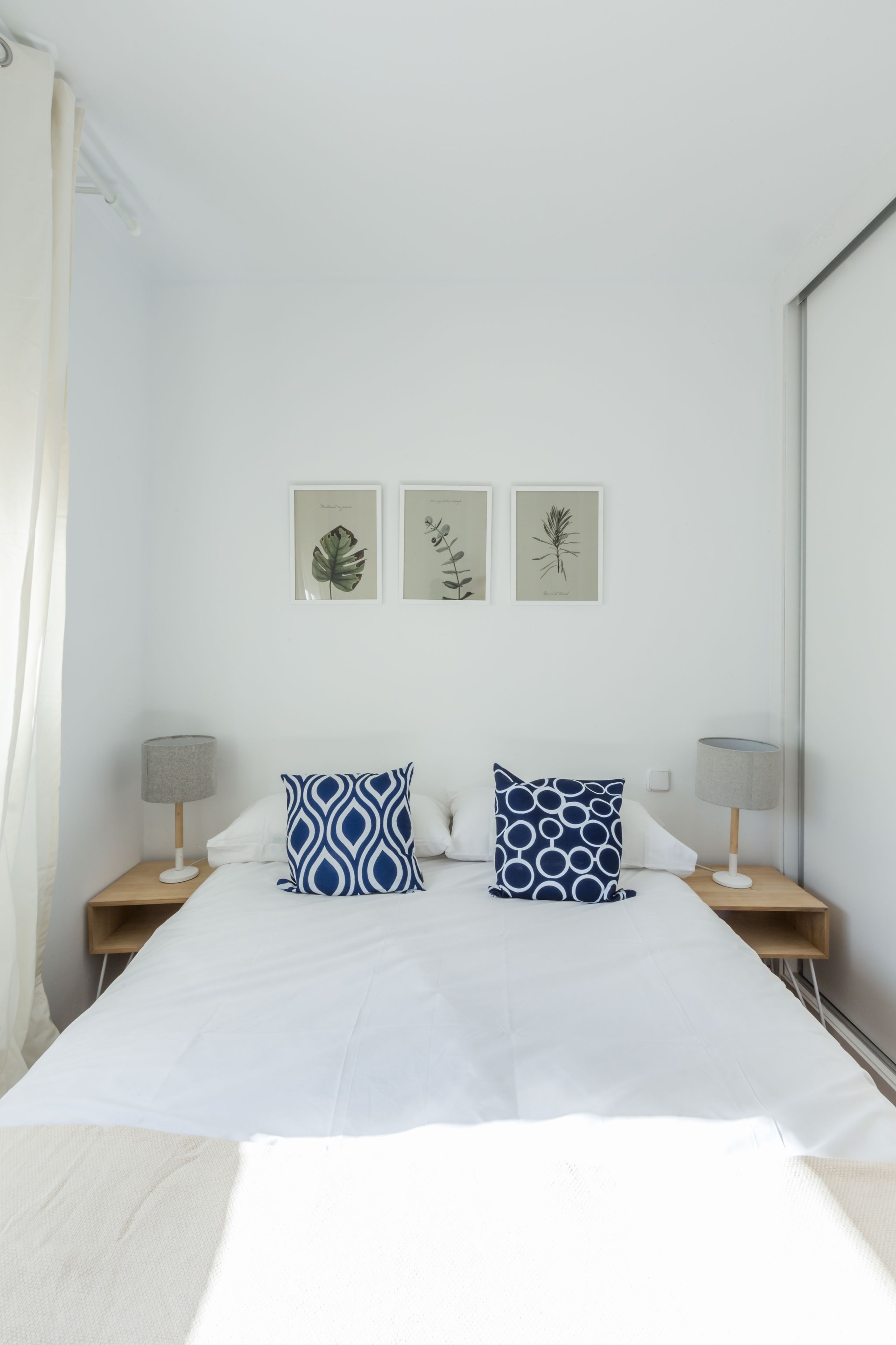 Une chambre avec un grand lit, deux tables de chevet et trois reproductions botaniques encadrées accrochées au mur.