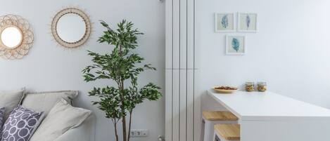 A modern, minimalist living space with a white sofa, a small plant, and a white dining area.