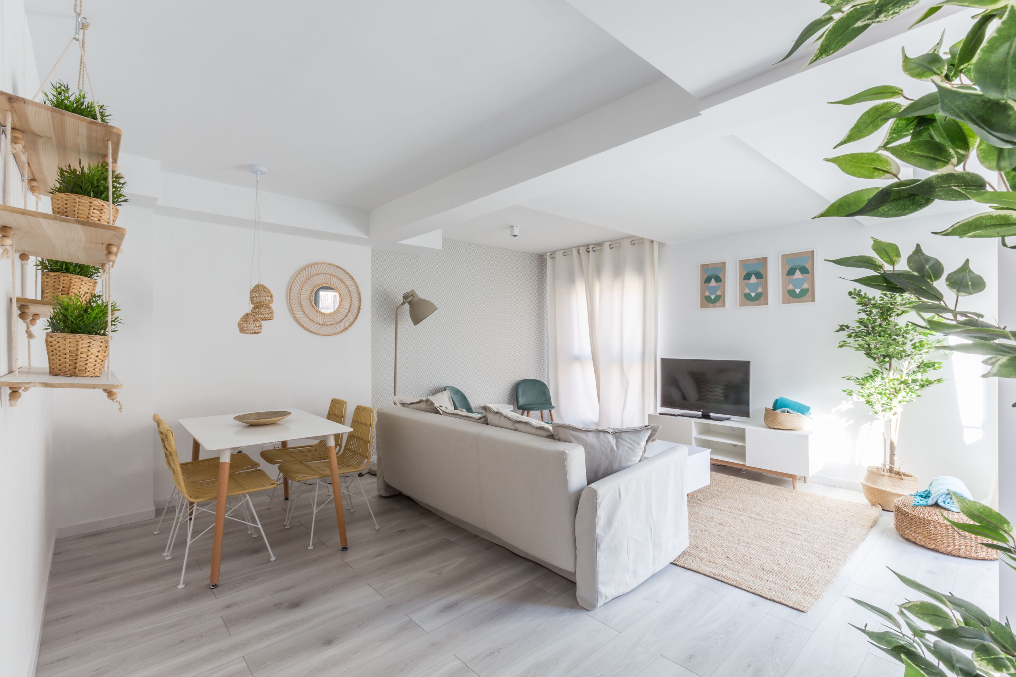 Een moderne woonkamer met een bank, een eettafel en stoelen, een televisie en een groot raam met gordijnen.