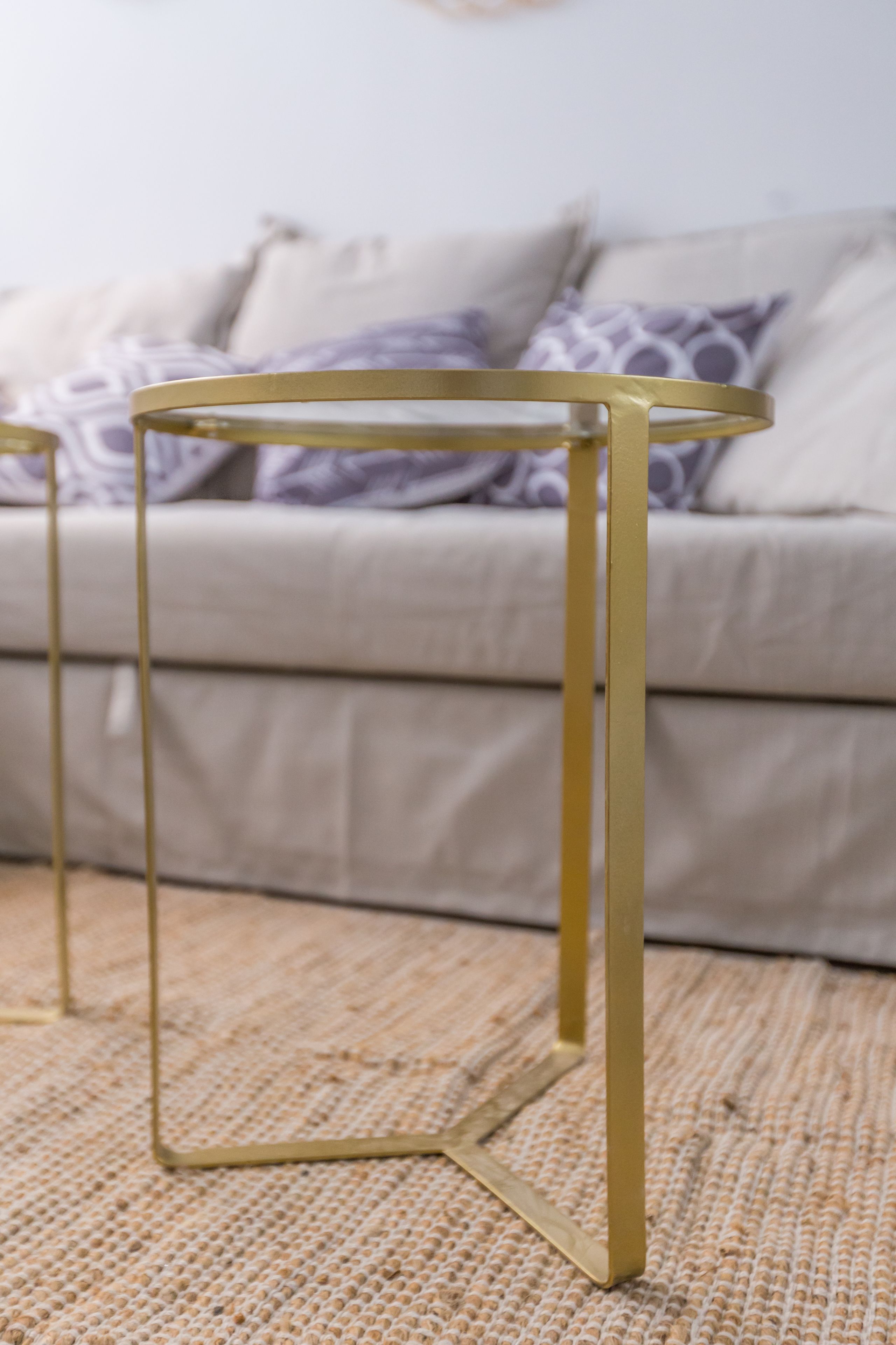 Een kamer met een beige bank, een kamerkleed met dessin en een bijzettafeltje met gouden lijst.