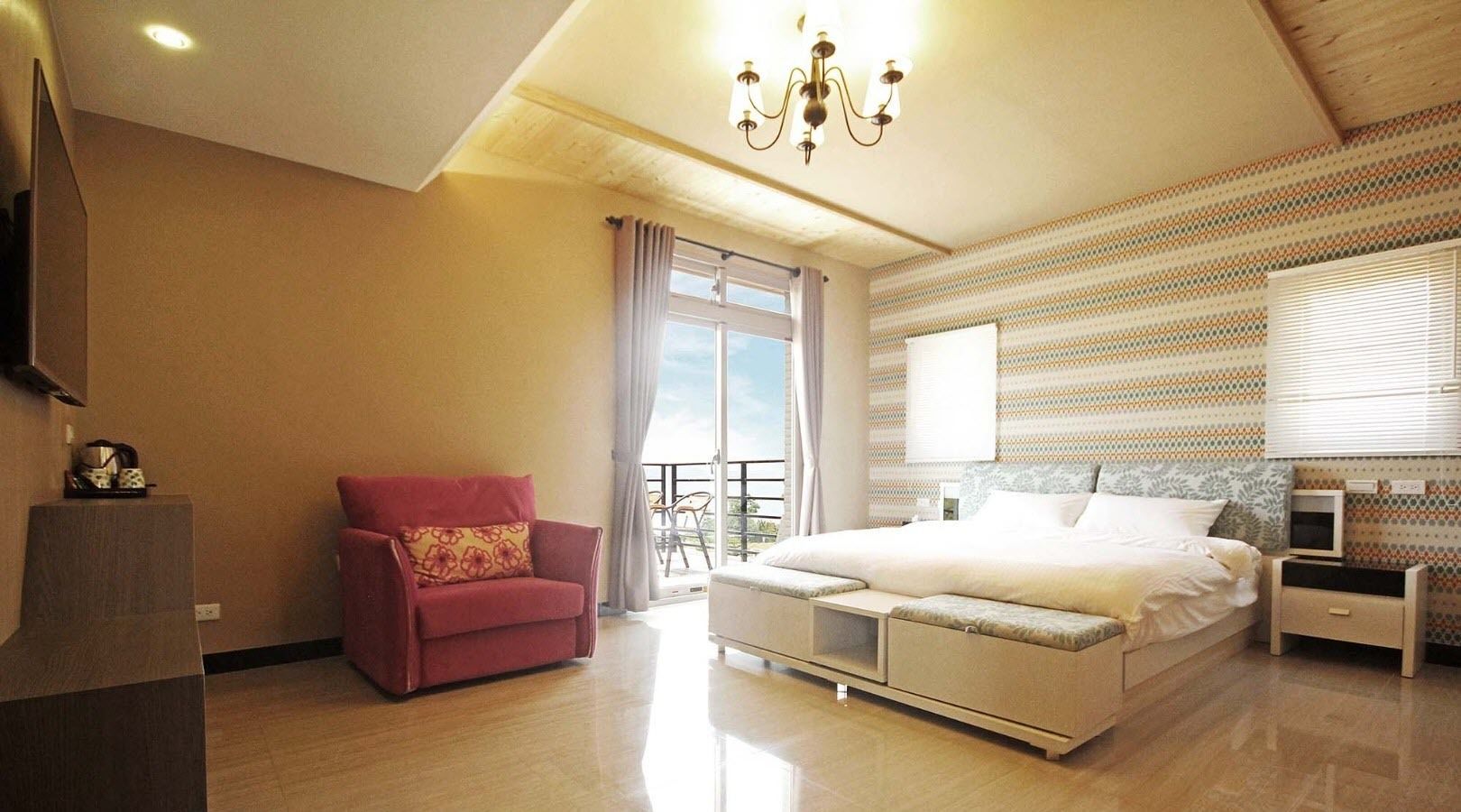 A modern bedroom with a large bed, a red armchair, and a balcony with a view.