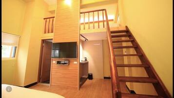 A compact room with a wooden staircase, a small seating area, and a television.
