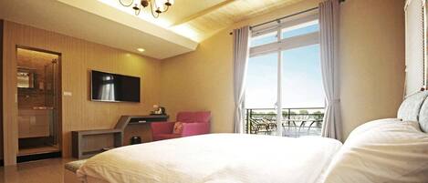A hotel room with a large bed, a TV mounted on the wall, a seating area with a chair, and a balcony with a view.