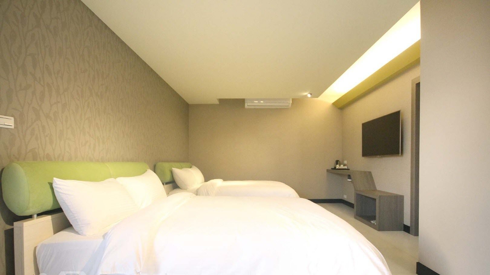 A hotel room with two beds, a flat-screen TV, and a small desk.