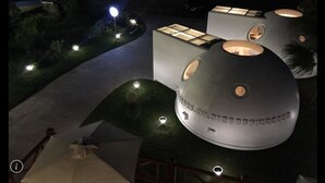 Un edificio moderno con estructuras esféricas que incluyen ventanas circulares, rodeado por un jardín ajardinado con senderos e iluminación.