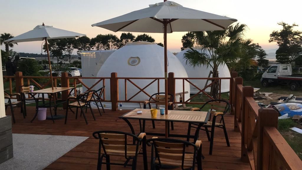 An outdoor deck with wooden tables and chairs, umbrellas, and a view of a dome-shaped structure.