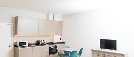 Eine moderne Küche mit Mikrowelle, Backofen und Kaffeemaschine, ein Essbereich mit blauen Stühlen, einer Couch und einem Flachbildfernseher auf einem Schrank.