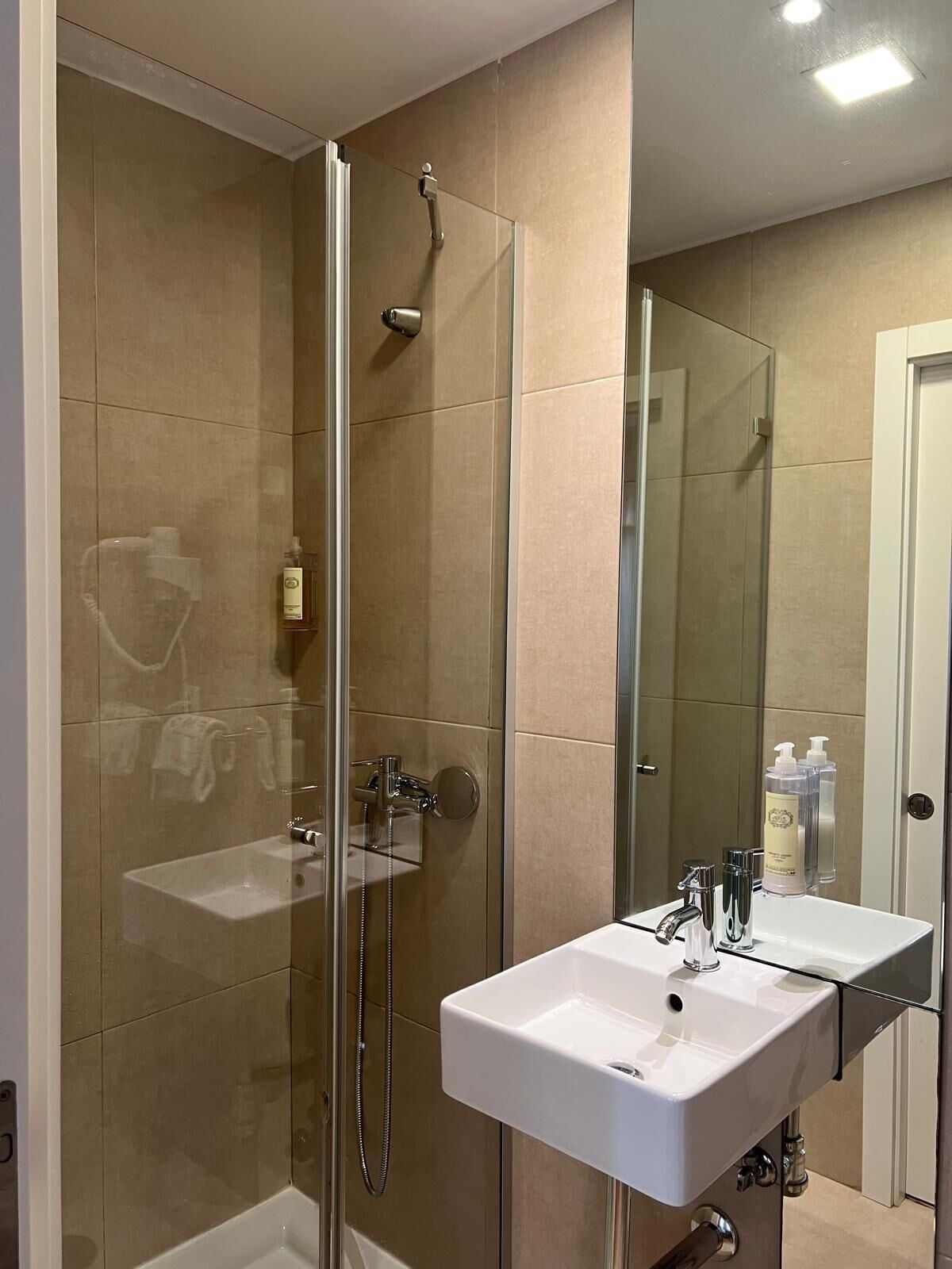 Een badkamer met een douche in een glazen cabine, een wit wastafelmeubel en een spiegel.