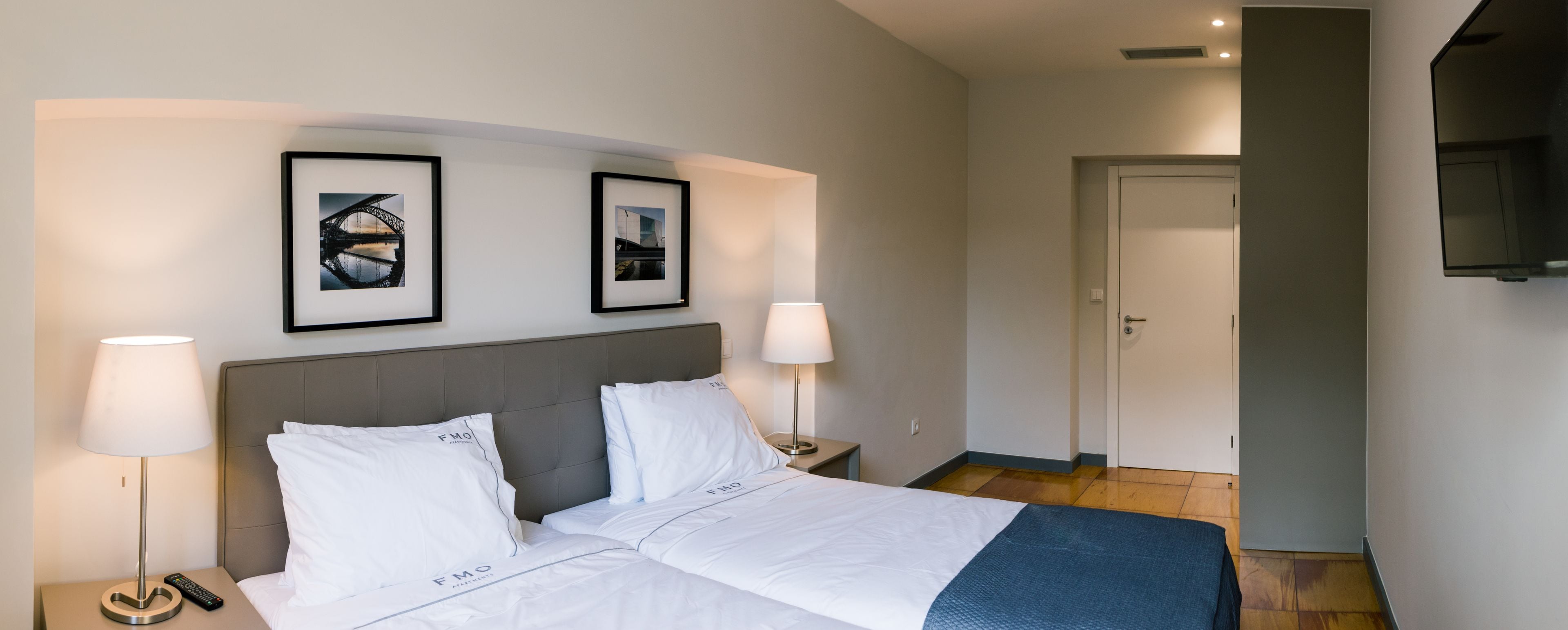 Una habitación de hotel con una cama, dos lámparas de noche, un control remoto y dos cuadros en la pared.