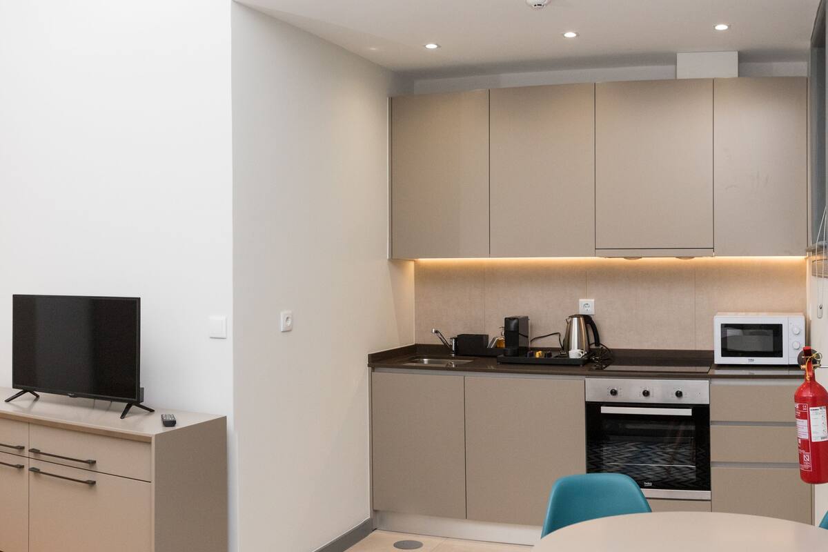 A compact kitchenette with a microwave, stove, and coffee maker. There is a TV on a small cabinet and a fire extinguisher mounted on the wall.