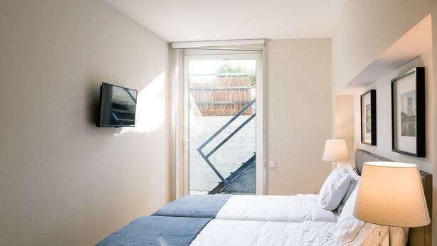 A bedroom with a bed, a TV mounted on the wall, a window with a view of a staircase, and a lamp on the bedside table. - FMO Apartments Boavista (Porto)