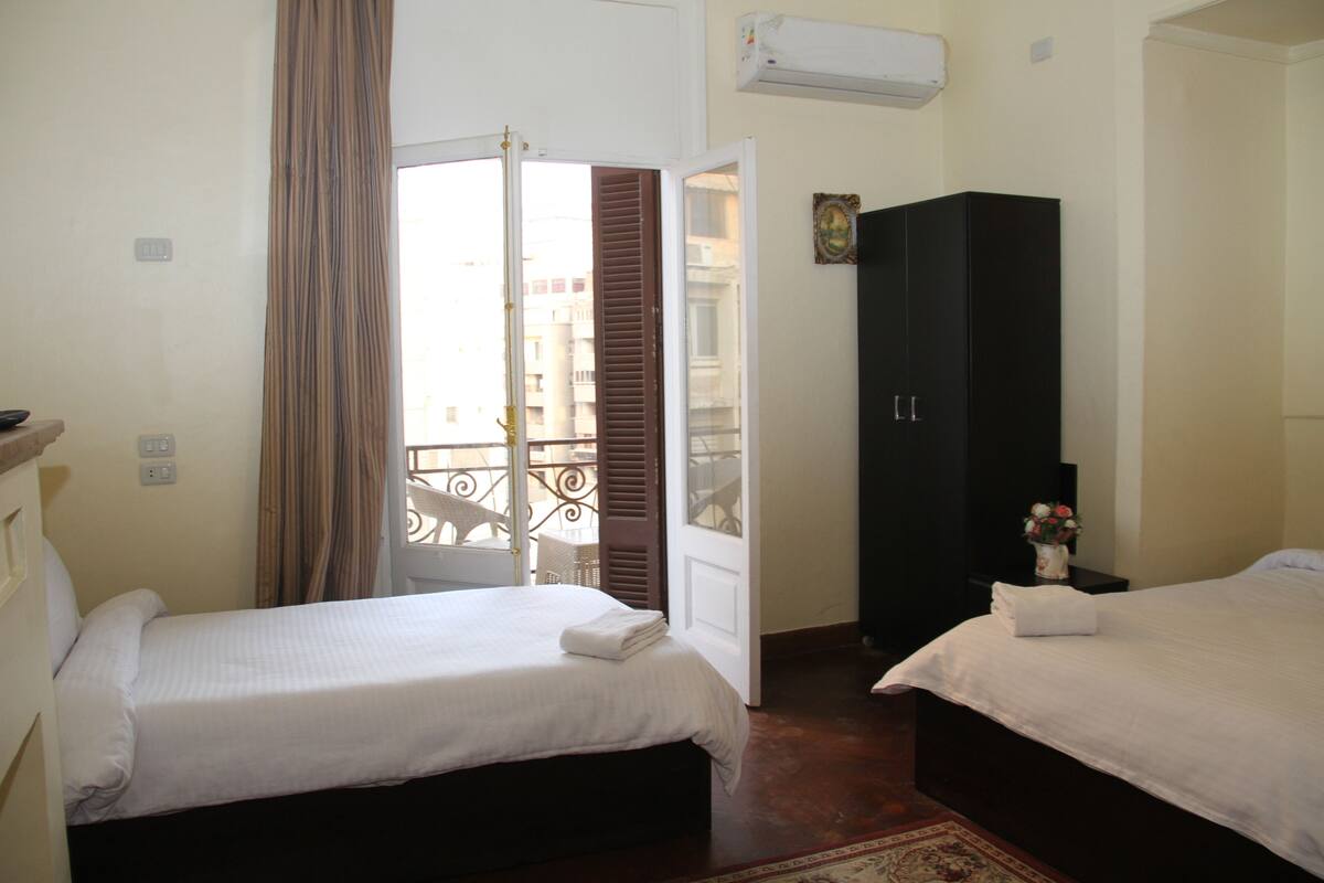 A hotel room with two beds, a wardrobe, an air conditioning unit, and a balcony with a view.