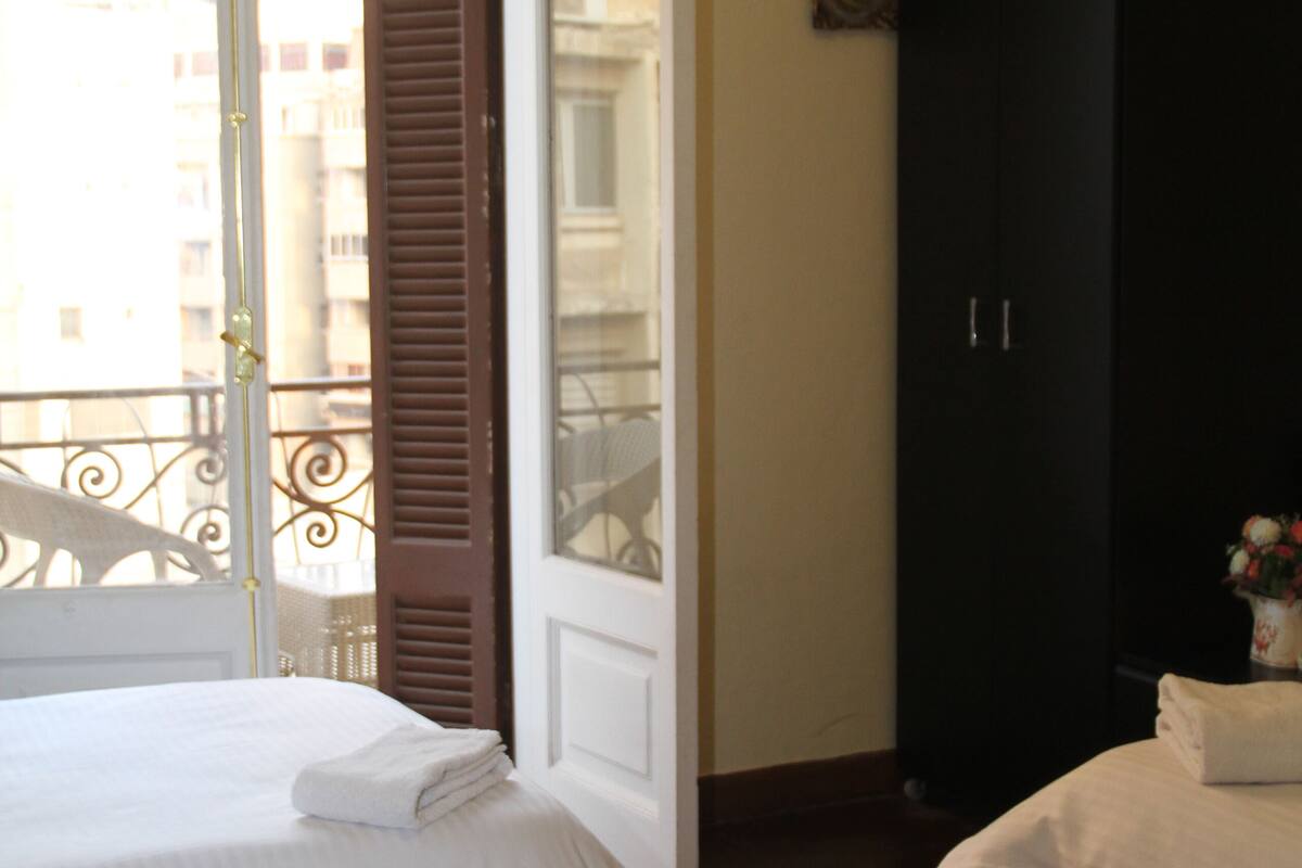 A bedroom with a bed, an open door to a balcony, a wardrobe, and a wall-mounted air conditioner.