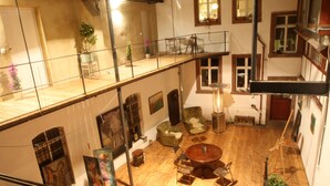 Ein geräumiges Loft mit Holzboden, einer erhöhten Zwischenebene und verschiedenen Sitzbereichen, darunter ein runder Tisch und gepolsterte Stühle.