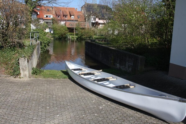 A canoe on a paved path beside a canal with buildings in the background.