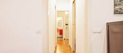 A narrow hallway with wooden flooring leading to a bathroom with a red towel hanging on the door.
