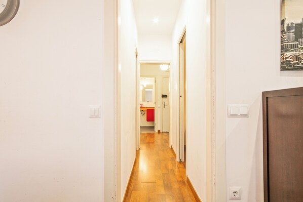 A narrow hallway with wooden flooring leading to a bathroom with a red towel hanging on the door. - Alcam Enamorats (Barcelona)