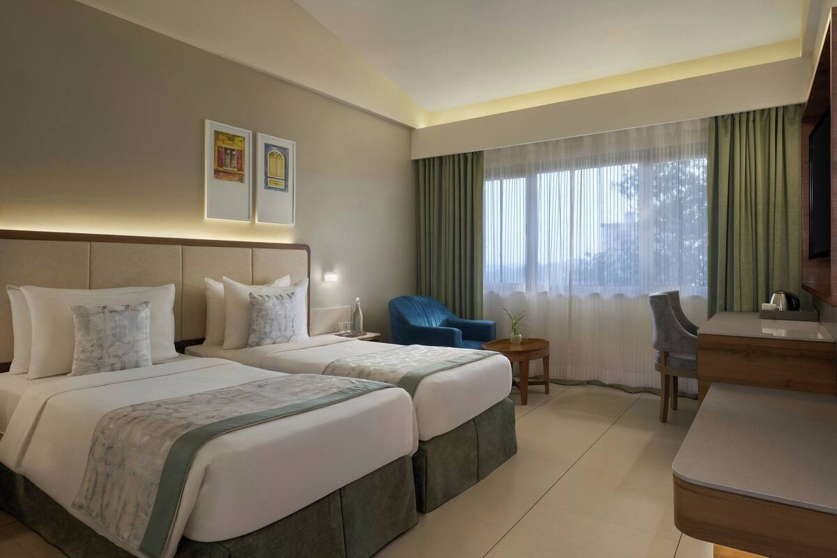 A hotel room with two beds, a desk, a chair, and a window with curtains.