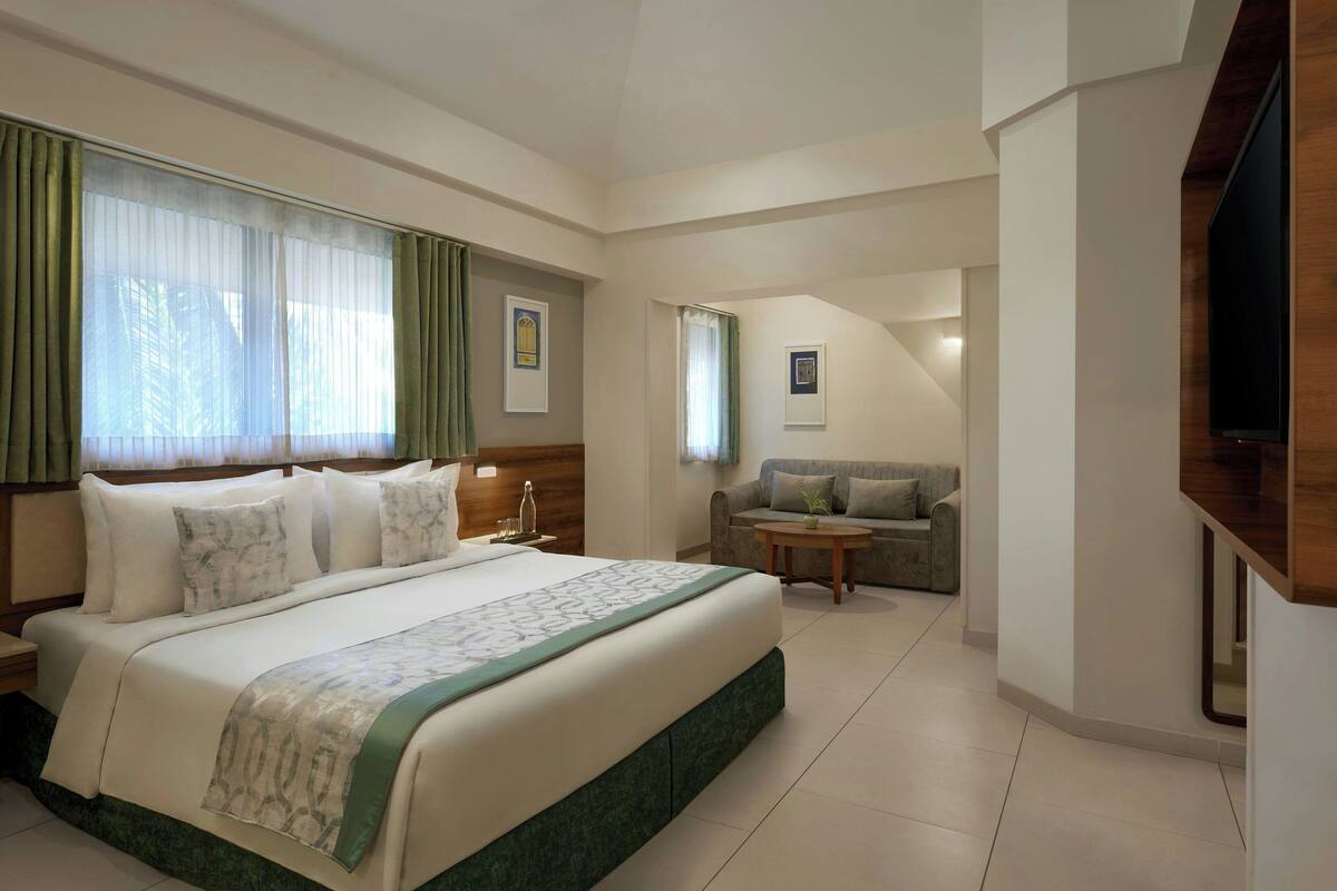 A hotel room with a large bed, a sofa, a small table, and a TV.