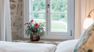 Ein Zimmer mit einem Bett, einem Fenster mit Blick ins Grüne und einer Vase mit Blumen auf der Fensterbank.