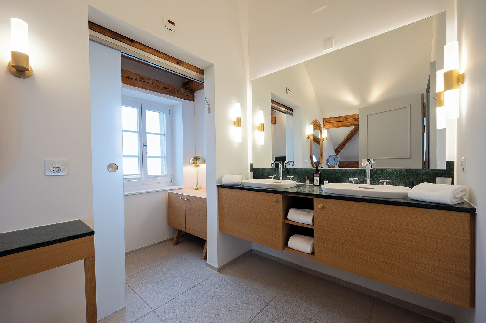 Ein modernes Badezimmer mit einem großen Spiegel, zwei Waschbecken, Holzschränken und einem Fenster.