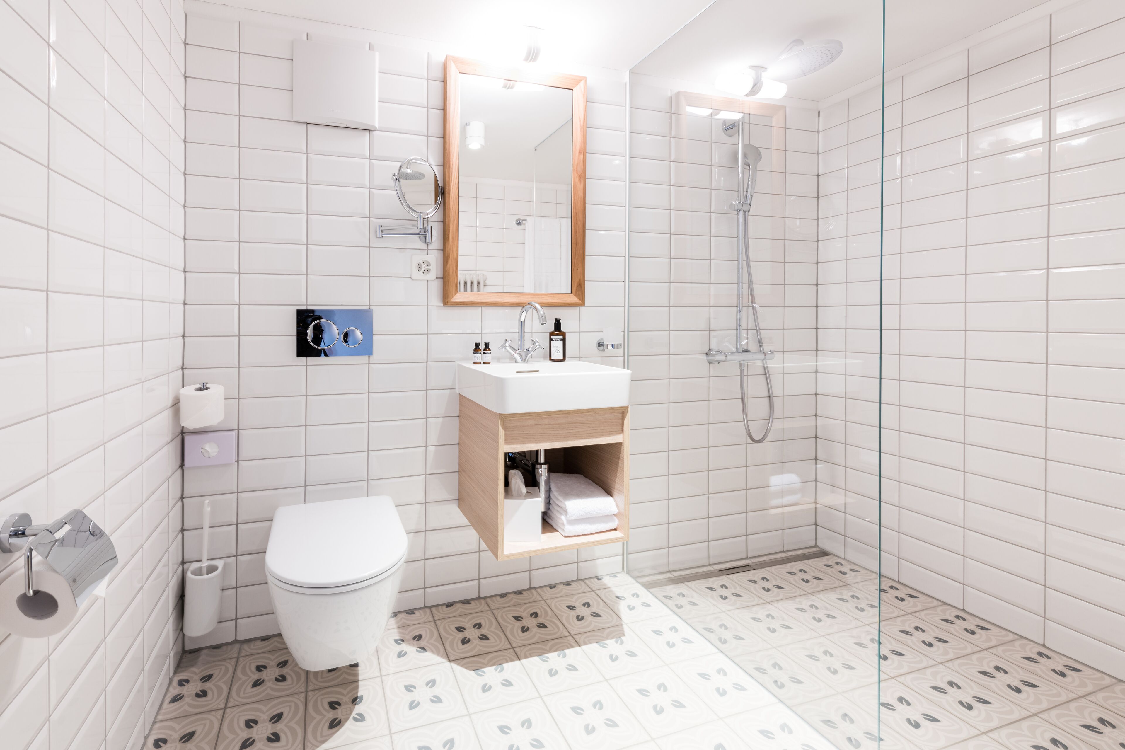 A modern bathroom with white tiles, a toilet, a sink with a mirror, and a shower.