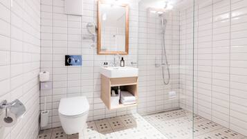 A modern bathroom with white tiles, a toilet, a sink with a mirror, and a shower.