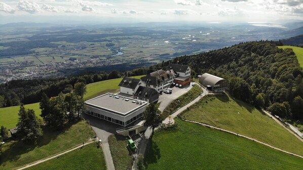 An aerial view of a building complex with multiple structures, surrounded by green fields and a river in the background. - Hotel Weissenstein (Oberdorf)