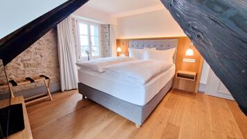 Un dormitorio con una cama grande, piso de madera, pared de piedra y una ventana con cortinas.