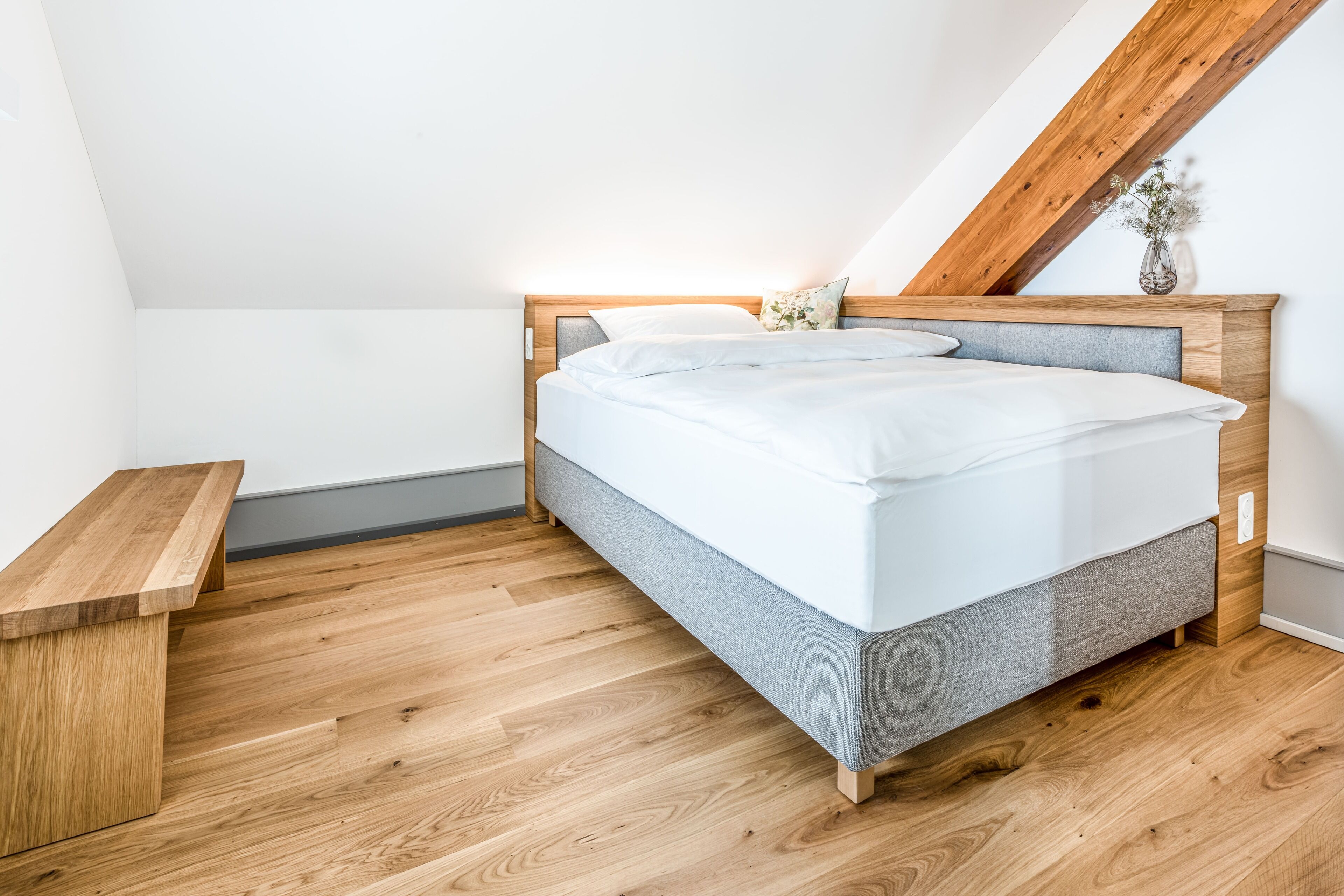 Une chambre à coucher avec un lit en bois, une tête de lit rembourrée de couleur grise et un banc en bois.
