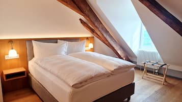 A bedroom with a wooden ceiling, a bed with white linens, two bedside lamps, and a radiator.