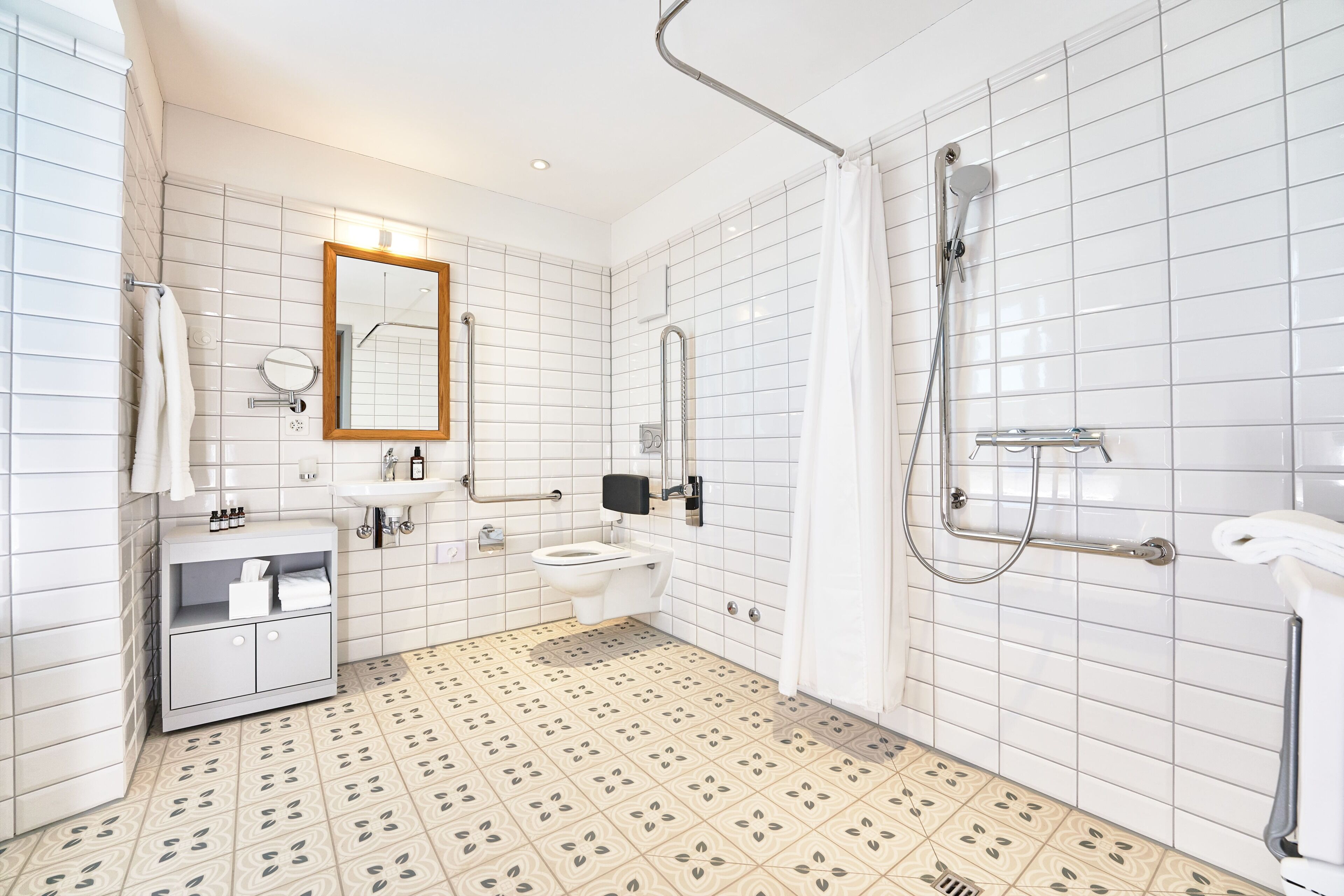 Un baño moderno con inodoro, lavamanos, espejo, ducha y suelo con baldosas estampadas.