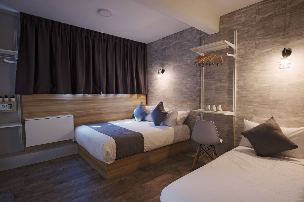 Quarto moderno com cabeceira de madeira, mesa de cabeceira, uma cadeira e prateleira embutida com artigos de higiene pessoal.