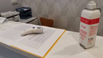 En receptionsdisk med en handspritdispenser, en digital termometer och en skrivtavla med dokument.