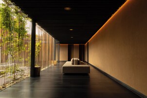 A corridor with a sofa, a wooden floor, and a glass wall with plants.