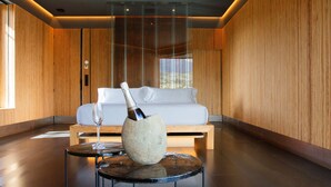 A modern room with a wooden panel wall, a white sofa, a stone vase with a bottle, and a glass on a small round table.
