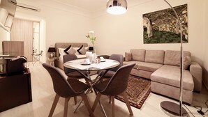 A modern living room with a round dining table, grey sofas, a floor lamp, and a painting on the wall. - Coladir Guest House (Rome)