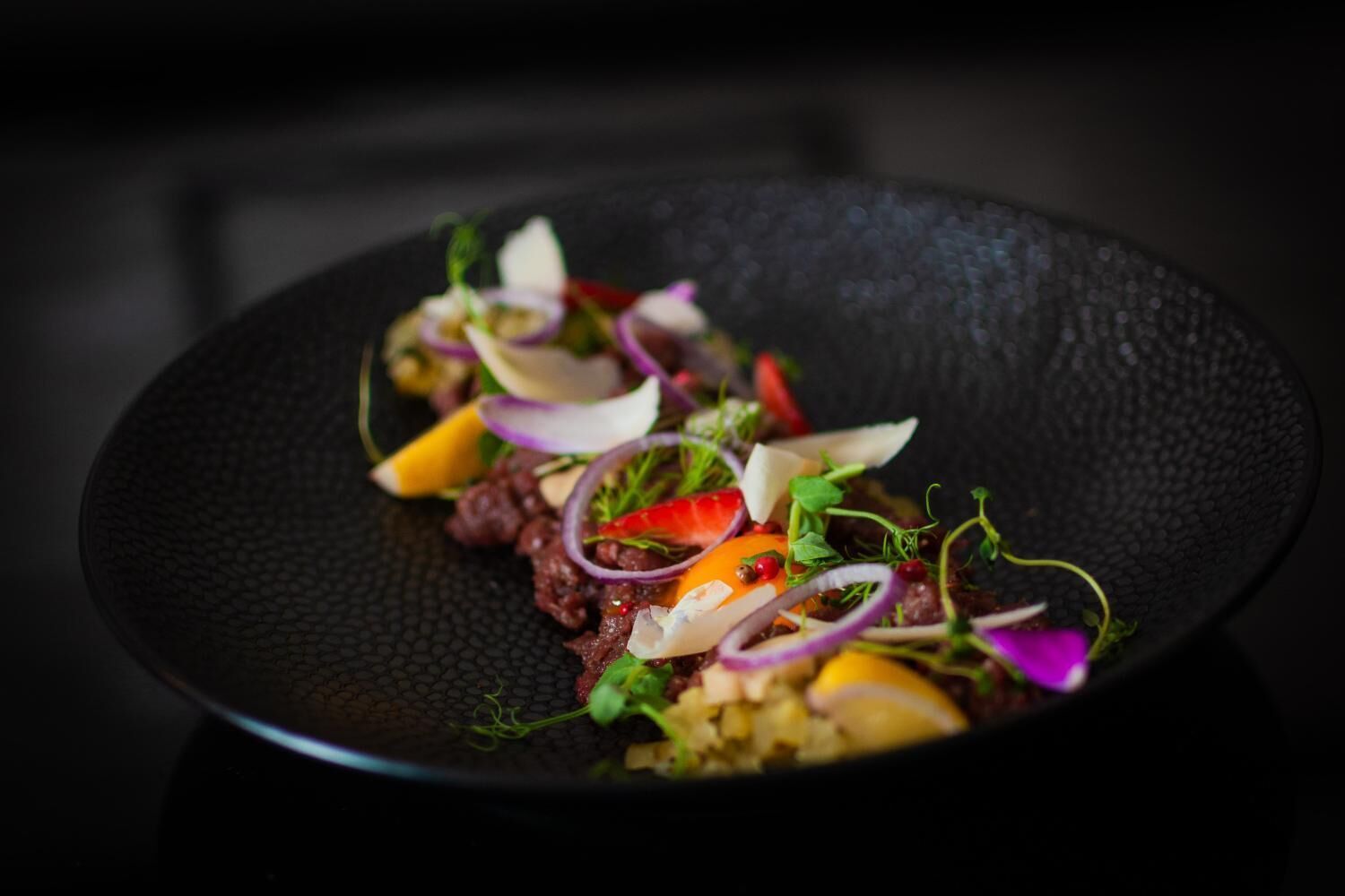 A dish with various ingredients on a black plate.