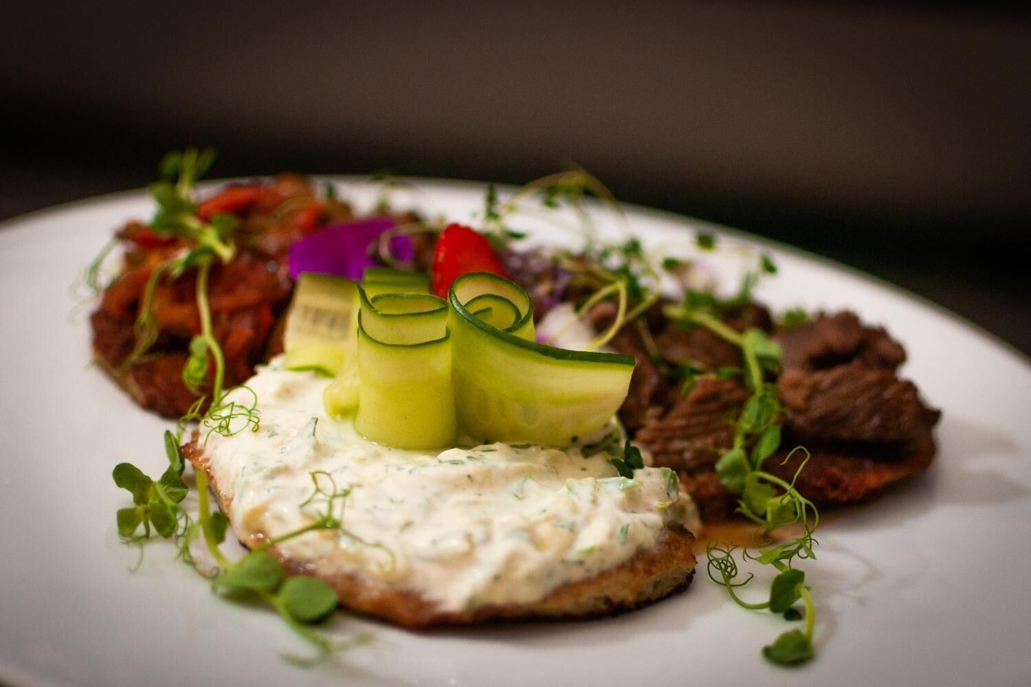 A plate with a variety of food items including a piece of meat, vegetables, and a creamy sauce.