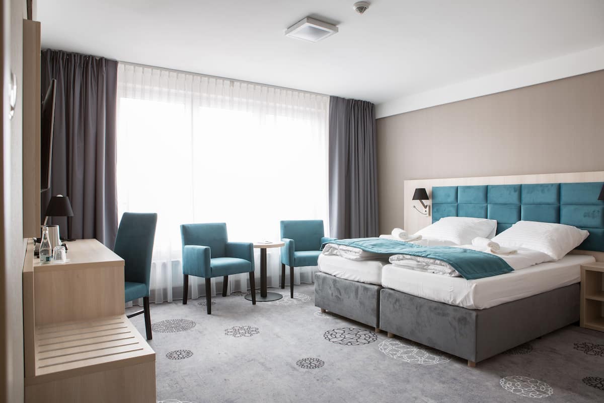 A hotel room with a bed, two chairs, a small table, and a desk.