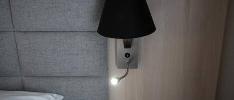 Quarto moderno com cabeceira estofada cinza, luminária preta fixada na parede e tomada.