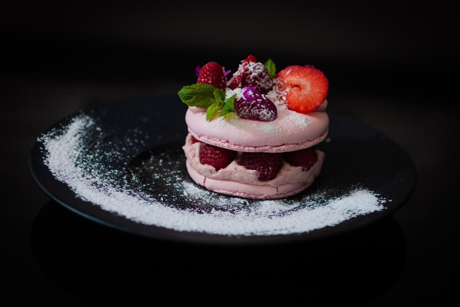 Dessert mit Erdbeeren und Minzblättern auf einer dunklen Platte.