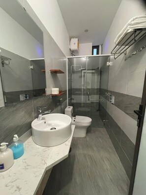 A modern bathroom with a round sink, toilet, and glass-enclosed shower. - Sapphire Hotel Hue (Hue)