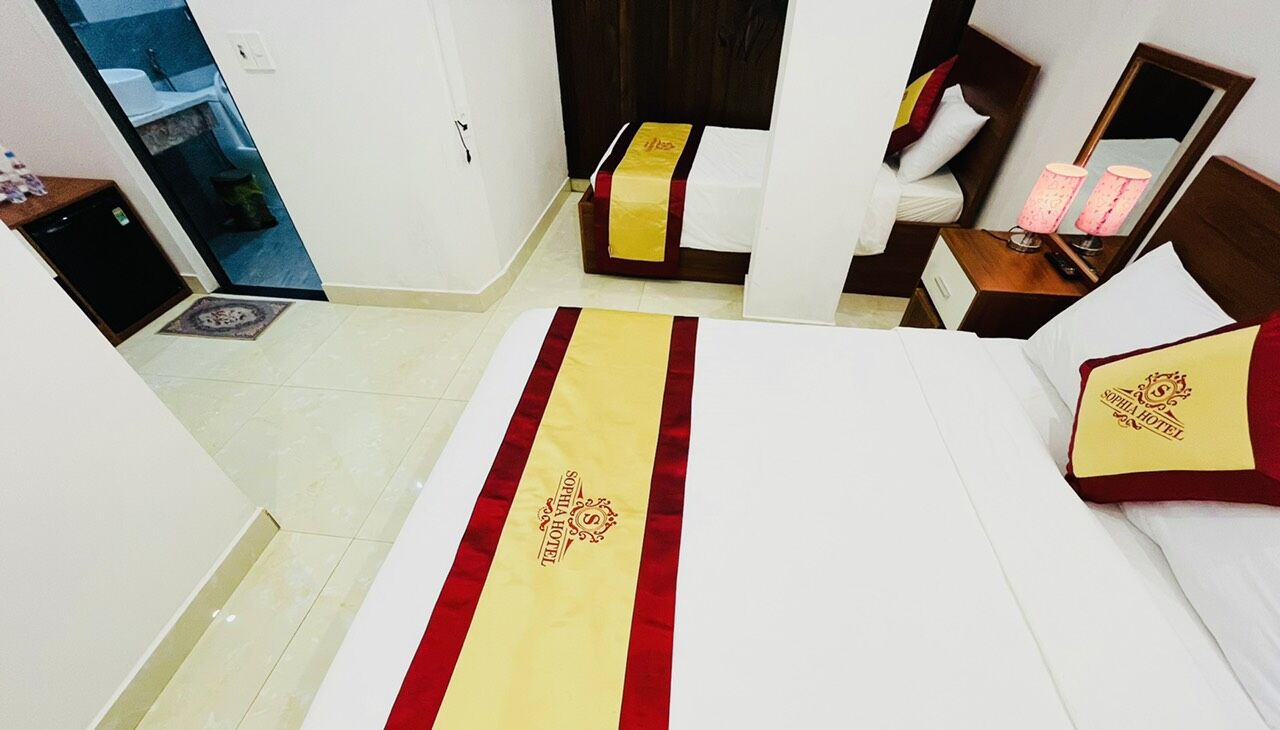 A hotel room with a bed, a bedside table with a lamp, a mirror, and a door leading to a bathroom.