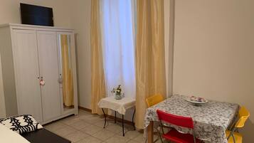 Una habitación pequeña y ordenada con cama, armario, mesa con sillas y ventana con cortinas.