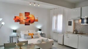 Een moderne hotelkamer met een bed, nachtkastjes, een glazen eettafel en een kitchenette.